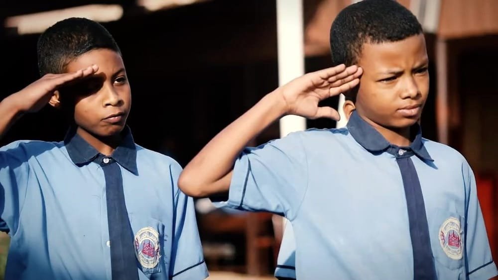 Two schoolboys in blue shirts salute. A frame from Sudan: This Land Is Ours.