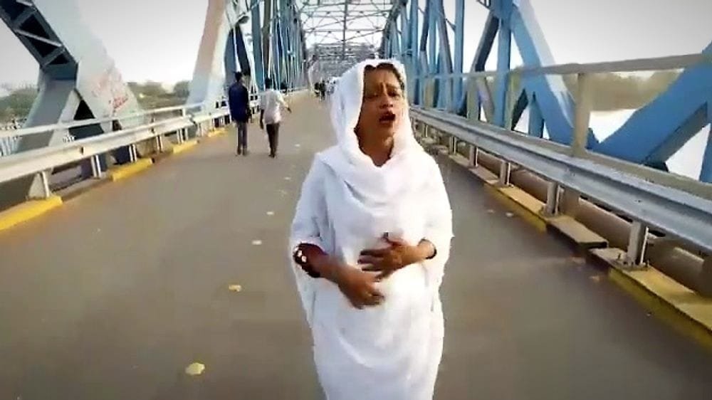 A woman in white walks across a steel bridge. A frame from Mona Magdi, A Free Sudanese Woman.