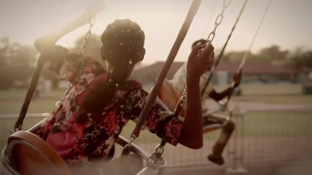 A girl in a red dress on a swing in warm evening light. A frame from Survivors.