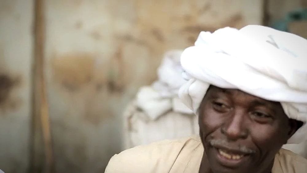 A smiling man in a white turban. A frame from We Are All Sudan.