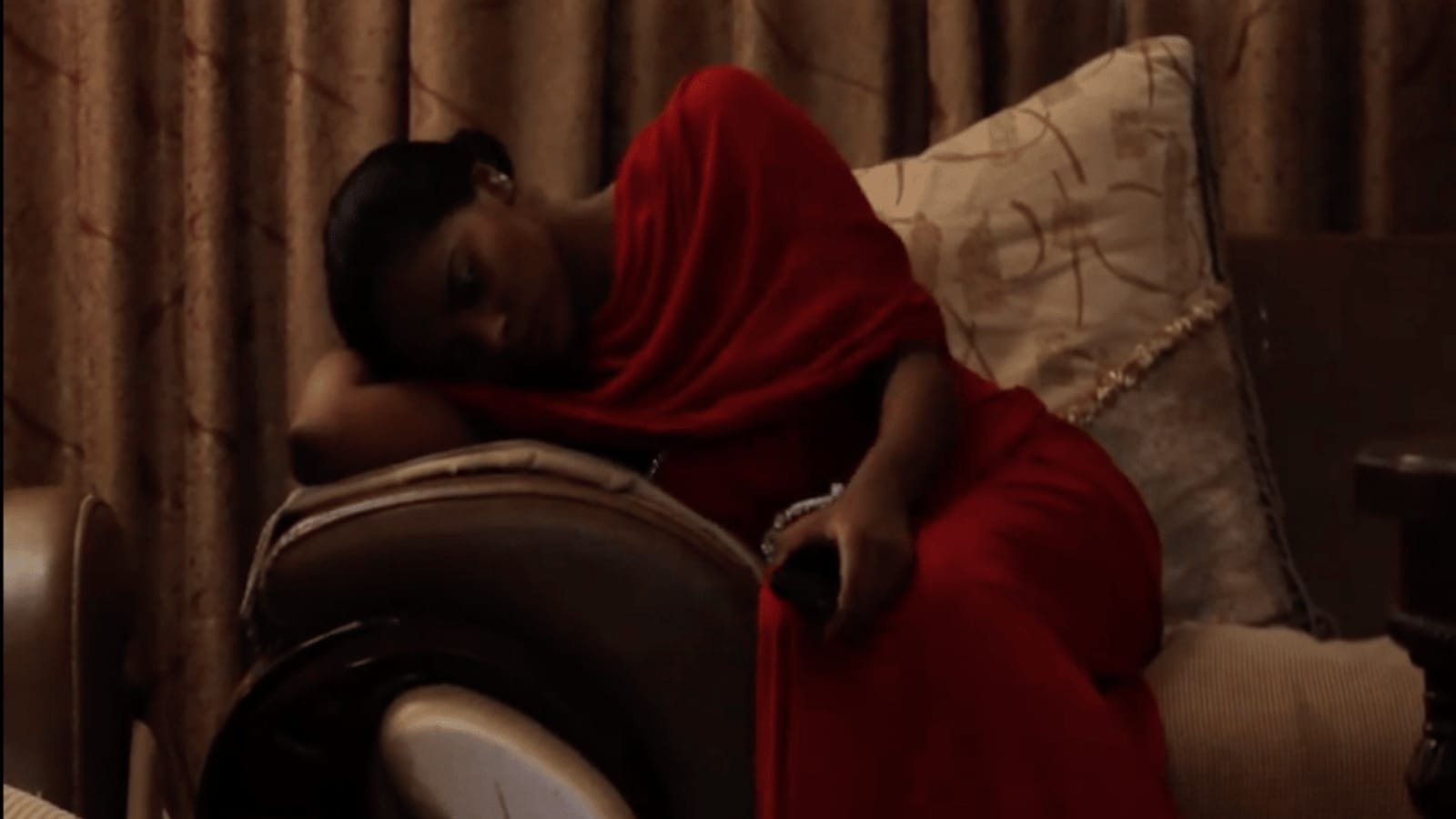 A woman in a deep red tobe resting on a sofa in warm lamplight. A frame from the short film Quronful.