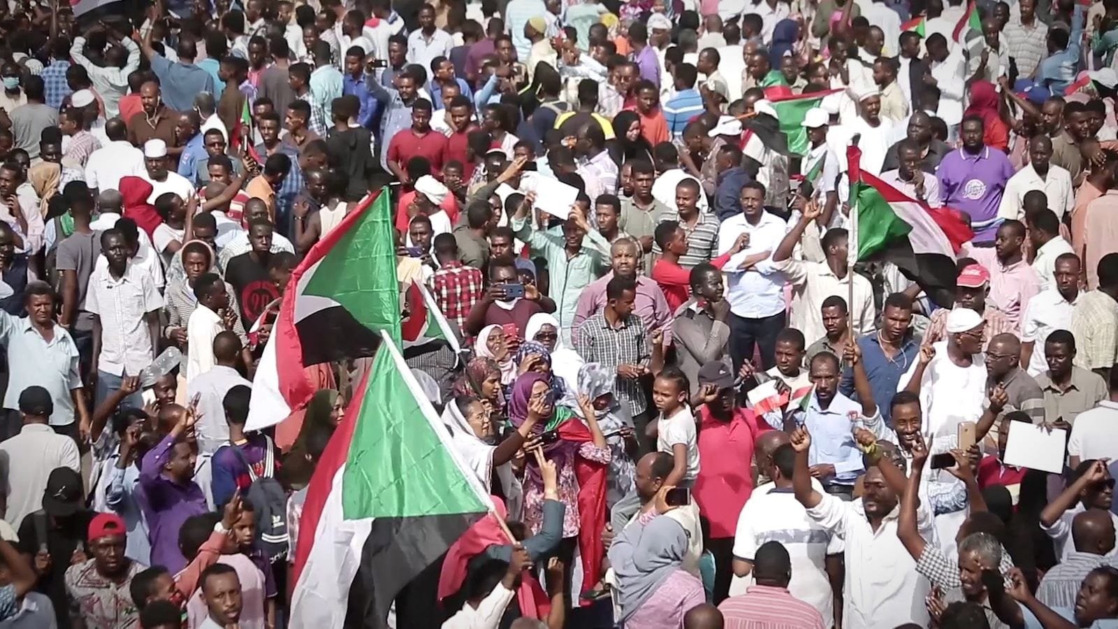 A huge crowd marches with Sudanese flags. A frame from Women of Sudan.