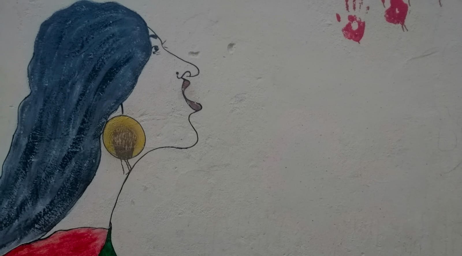 A street mural in Sudan: a woman in profile with long dark hair and a gold earring calls out, her shoulder painted in the colours of the Sudanese flag. Red handprints are pressed into the wall beside her.