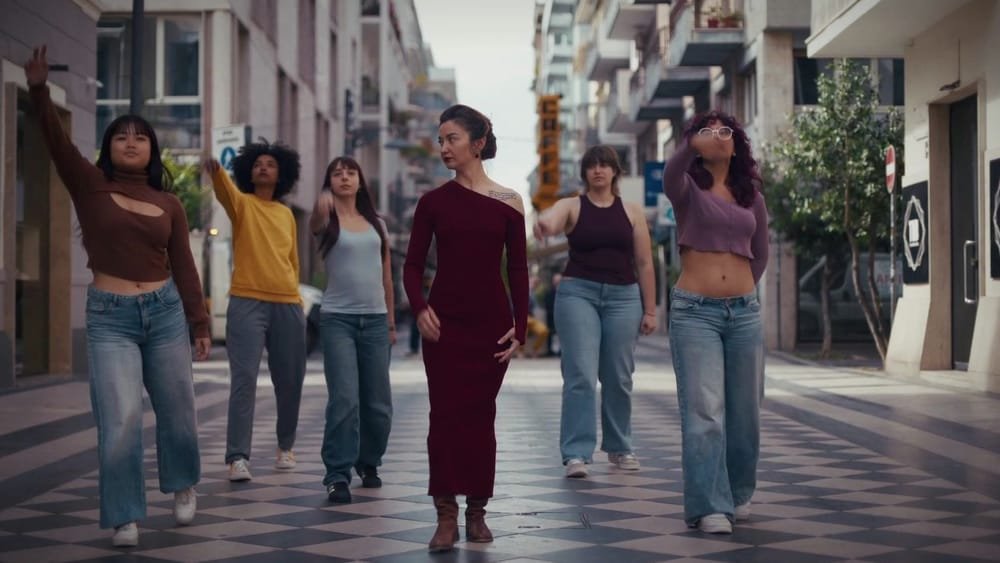 Six young women walk side by side down a shopping street. A frame from My Way.